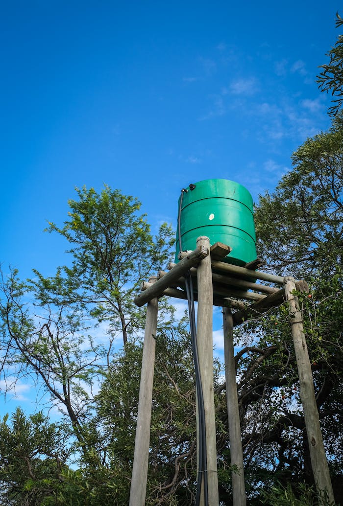 A photo of an elevated green water tank supported by a wooden frame, set against a clear blue sky.