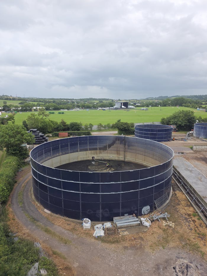 Overhead shot of large round water storage tanks in a green landscape.
